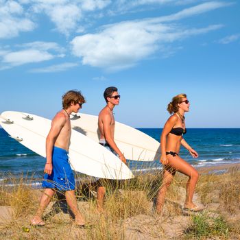 Surfer teen boys and girl group walking on dune way to beach on summer