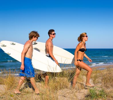 Surfer teen boys and girl group walking on dune way to beach on summer