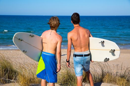 Boys teen surfers rear back view looking at beach from uo dune