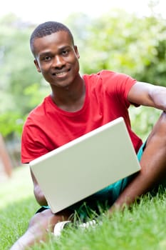 young smiling african student sitting in grass with notebook outdoor in summer man