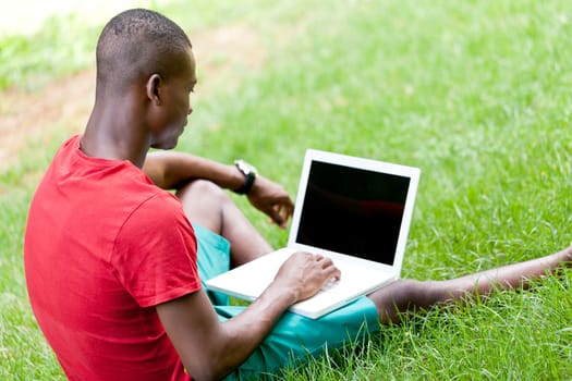 young smiling african student sitting in grass with notebook outdoor in summer man