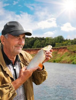 chub in the hand of fisherman against the sky and the river
