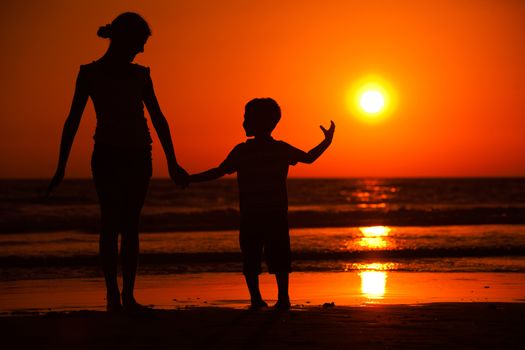 Silhouette of little brother and sister playing at the beach during sunset