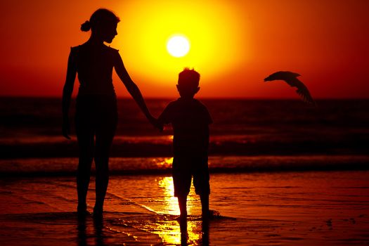 Silhouette of little brother and sister playing at the beach during sunset