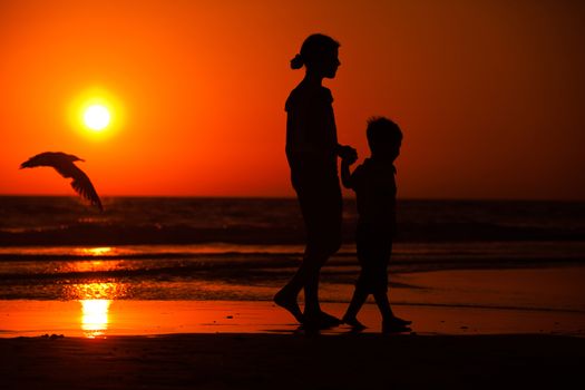 Silhouette of little brother and sister playing at the beach during sunset