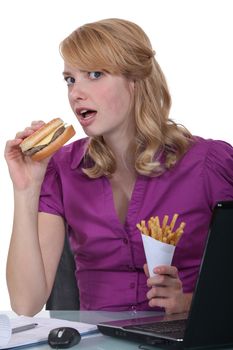 Woman eating burger and fries at desk