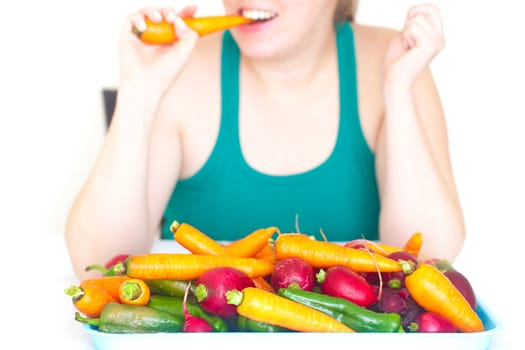 young woman eating a carrot and a heap of vegetables 