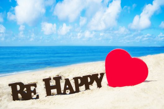 Sign "Be Happy" and heart shape on the sandy beach by the ocean in sunny day