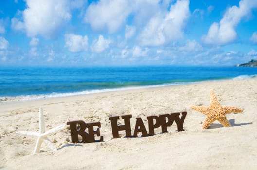Sign "Be Happy" and two starfishes on the sandy beach by the ocean in sunny day