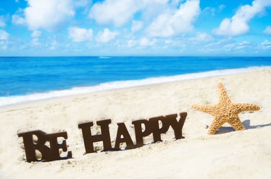 Sign "Be Happy" and starfish on the sandy beach by the ocean in sunny day
