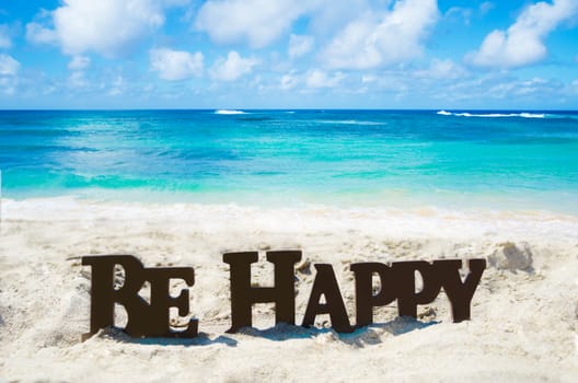 Sign "Be Happy" on the sandy beach by the ocean in sunny day