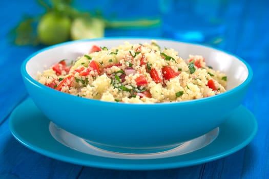 Fresh homemade Tabbouleh, an Arabian vegetarian salad made of couscous, tomato, cucumber, onion, garlic, parsley and lemon juice served in a blue bowl (Selective Focus, Focus one third into the tabbouleh)