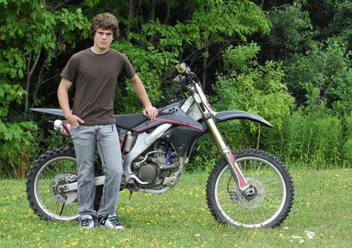 attractive teenage boy standing beside dirt bike 