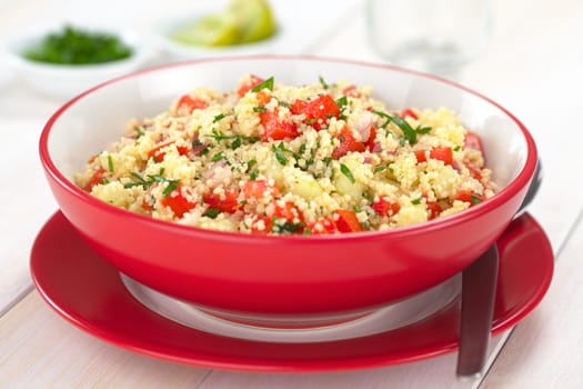 Fresh homemade Tabbouleh, an Arabian vegetarian salad made of couscous, tomato, cucumber, onion, garlic, parsley and lemon juice served in a red bowl (Selective Focus, Focus one third into the tabbouleh)