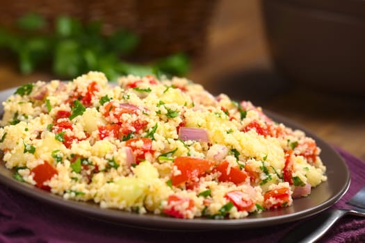 Fresh homemade Tabbouleh, an Arabian vegetarian salad made of couscous, tomato, cucumber, onion, garlic, parsley and lemon juice served on a brown plate on dark wood (Selective Focus, Focus one third into the tabbouleh)