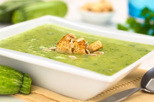 Zucchini cream soup with wholewheat croutons and roasted sunflower seeds served in white bowl (Selective Focus, Focus on the front of the croutons) 