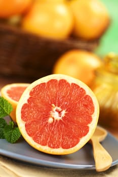 Half of a pink-fleshed grapefruit on blue plate with mint leaf and wooden spoon (Very Shallow Depth of Field, Focus on the middle of the grapefruit half)