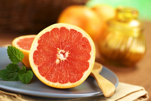 Half of a pink-fleshed grapefruit on blue plate with mint leaf and wooden spoon (Very Shallow Depth of Field, Focus on the middle of the grapefruit half)