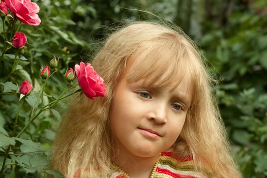 Beautiful little Caucasian girl in park near the rose bush