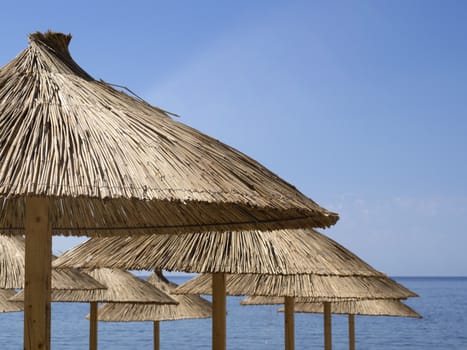 many straw sunshade parasols over blue sky and sea background with focus on front parasol