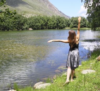 Young beautiful girl in a dress admires the mountain lake