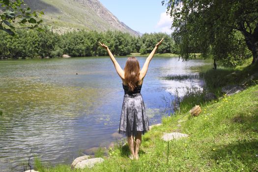 The young girl meditates on the shore of a mountain lake