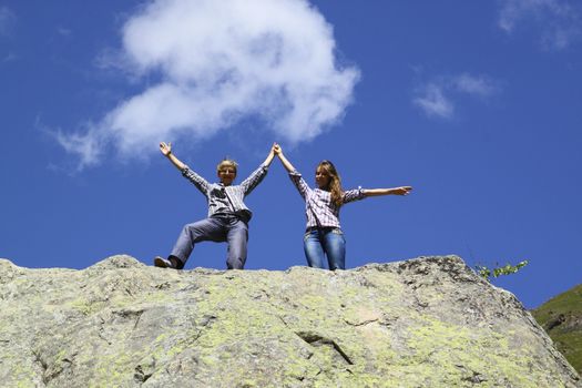 Happy mother and daughter standing on a huge rock, raising his hands up