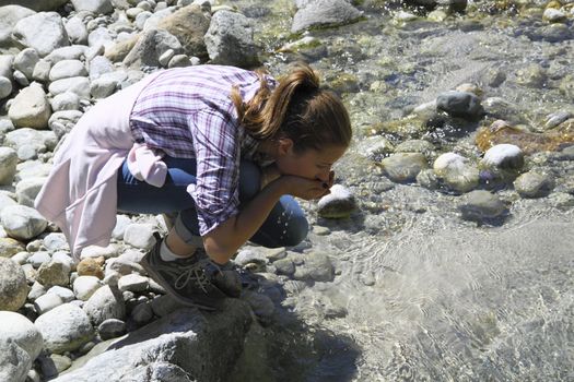 A young girl drinks pure water from a mountain stream