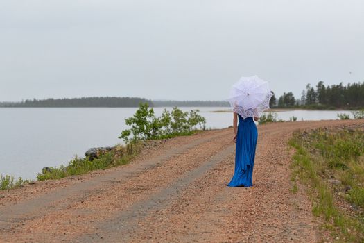 Slim girl in a dress with an umbrella in a forest on a country road