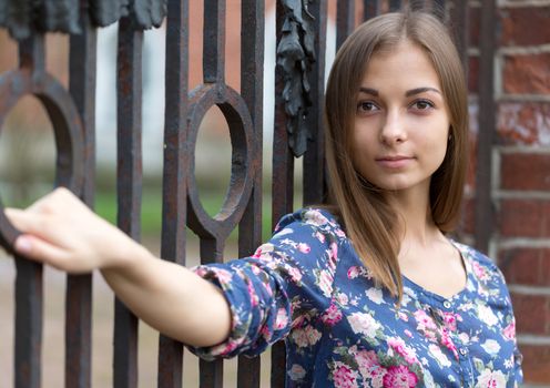 Portrait of a beautiful girl near the old rusty wrought fence.