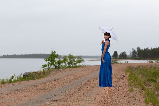 Beautiful girl in a blue dress with an umbrella on a country road