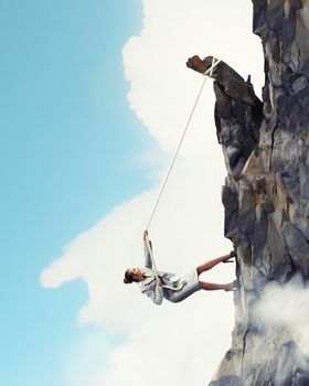 businesswoman climbing steep mountain hanging on rope