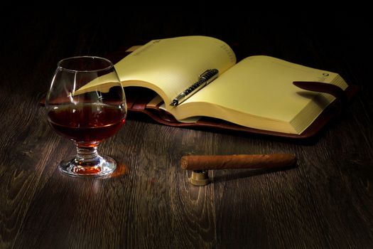 A glass with cognac, cigar and an old book nearby