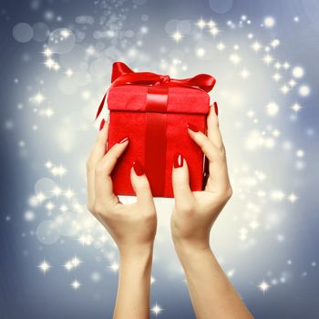 Woman's hands holding up red present box on Christmas on shinning background