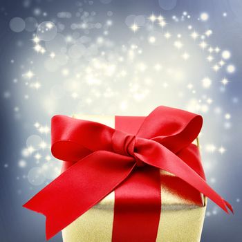 Golden present box with big red ribbon for Christmas on a shinning background