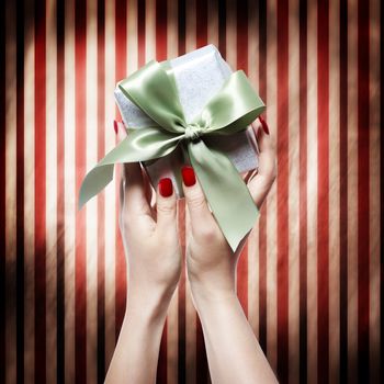 Hand with red nails holding a gift box over striped background
