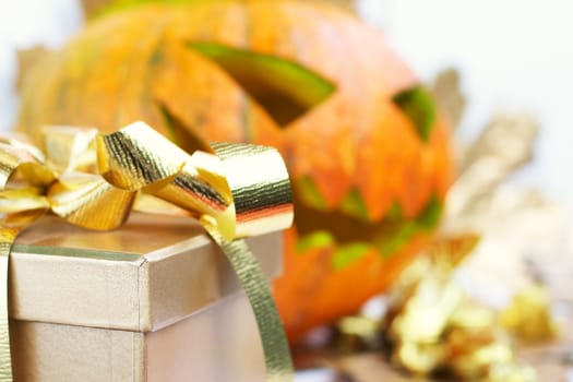 Halloween pumpkin with autumn leafs and gift close-up