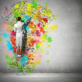 Back view of businesswoman drawing colorful business ideas on wall