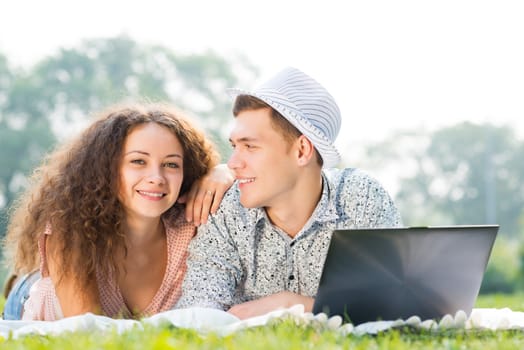 couple lying together in a park, working together on a laptop