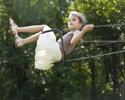 Happy little girl riding on a swing in the park