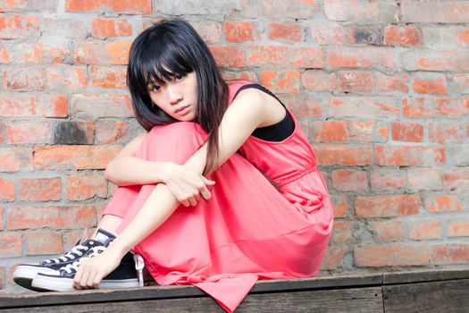 Young Asian woman sitting by red brick wall feeling depressed and sad