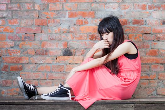 Young Asian woman sitting by red brick wall feeling depressed and sad