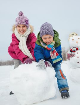 Happy beautiful children building snowman outside in winter time