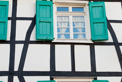 Shuttered window in an ancient timber frame house in Germany with pretty green shutters and lace curtains exterior architectural background