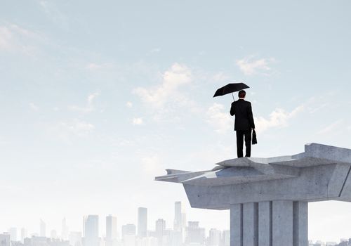 Image of businessman with umbrella standing at the edge of bridge