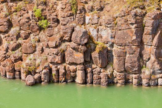 Close-up of weathered geologic basalt rock cliff wall of Miles Canyon with water of Yukon River  Yukon Territory  Canada
