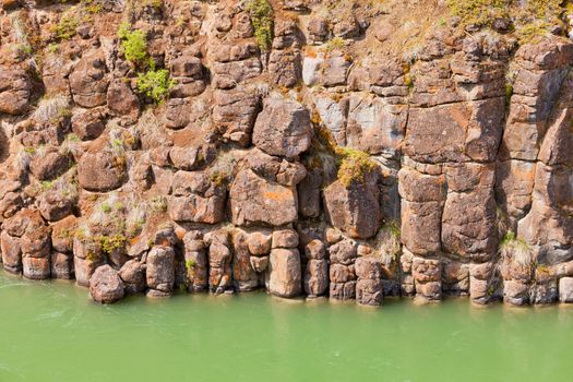 Close-up of weathered geologic basalt rock cliff wall of Miles Canyon with water of Yukon River Yukon Territory Canada