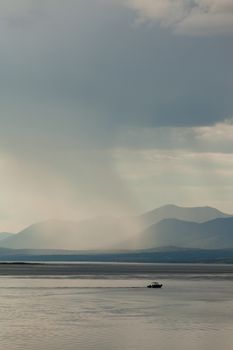 Heavy rain shower over Marsh Lake Yukon Territory Canada and distant mountain range with a small motorboat out on tranquil water