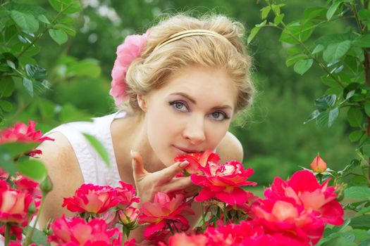 Sensual woman in pink rose garden smelling