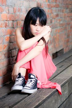 Young Asian woman sitting by red brick wall feeling depressed and sad